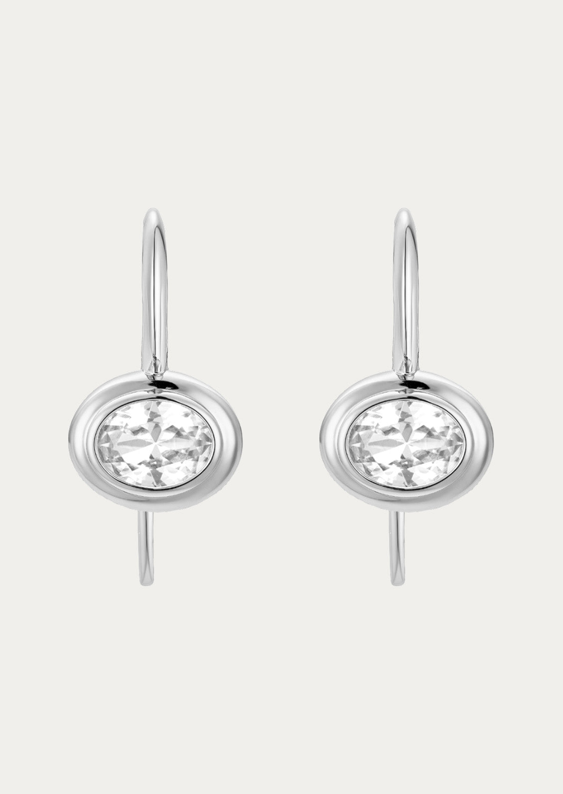 A pair of rhodium plated dangling hook earrings with a clear lab grown sapphire in the center on a white background.