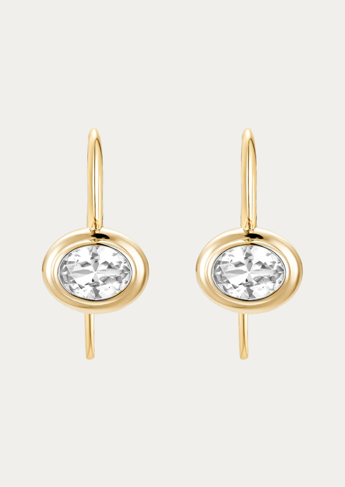 A pair of gold dangling hook earrings with a clear lab grown sapphire in the center on a white background.