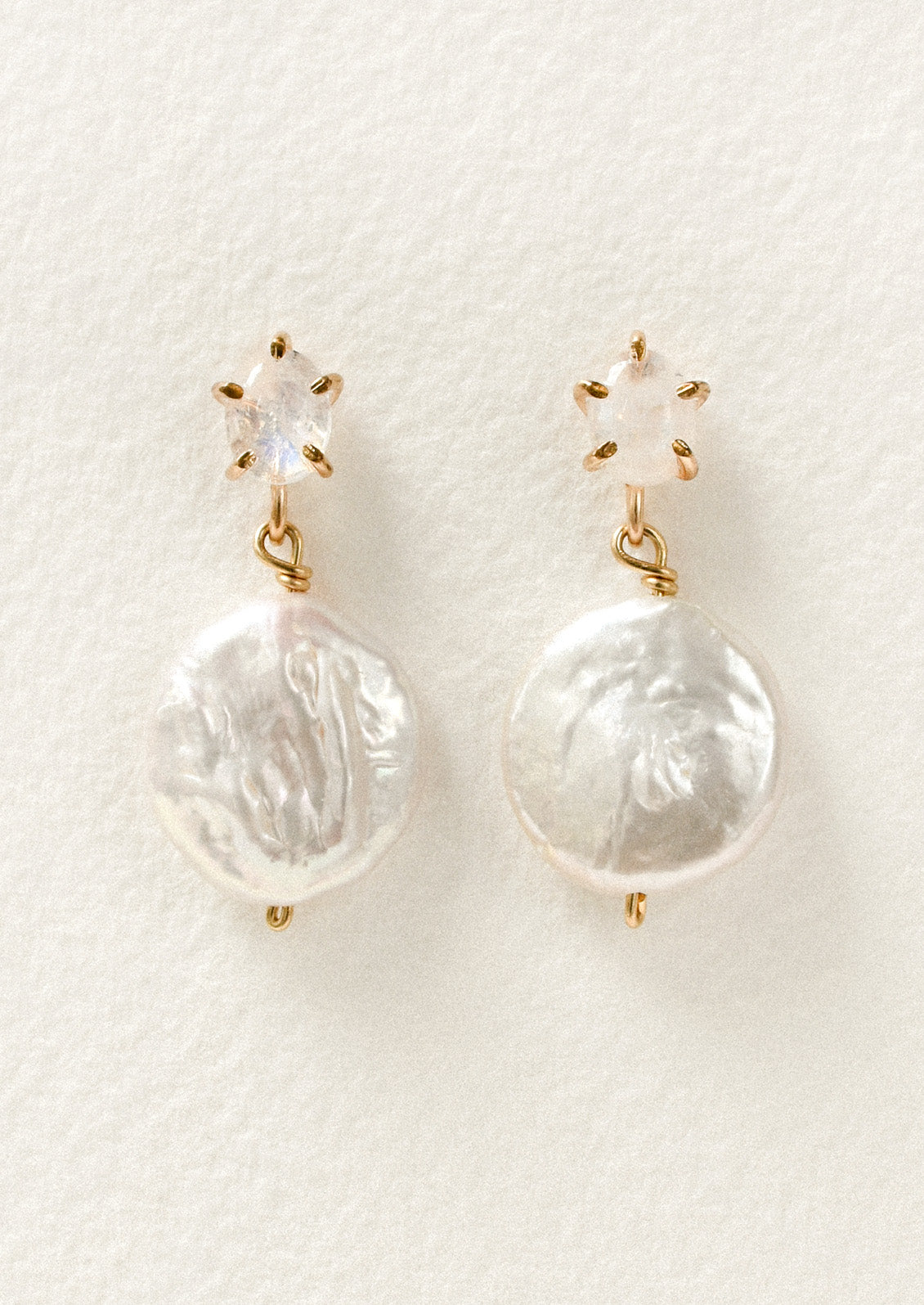 A pair of gold stud earrings feature a moonstone in a pronged setting with a large dangling freshwater coin pearl hanging below.