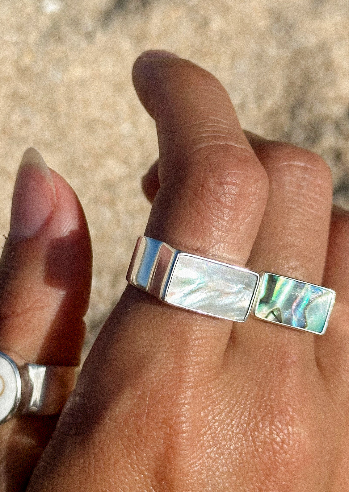 A hand wearing various rings including a sterling silver ring with a thick band and a rectangular mother of pearl set in the center.