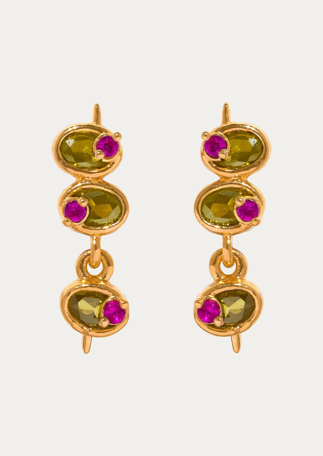 A pair of long gold stud earrings in the shape of olives with green and pink gems on a white background.