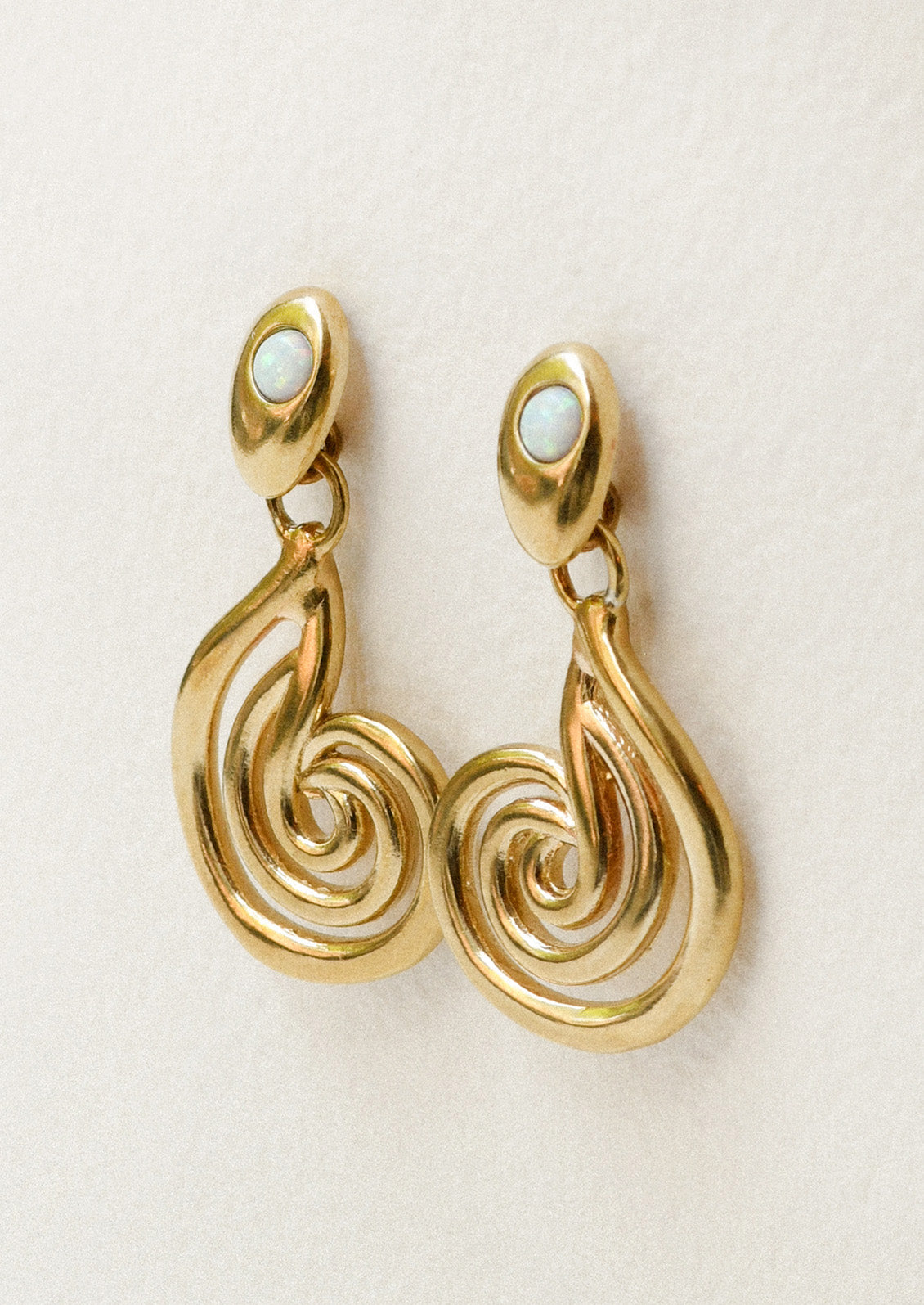 A pair of bronze earrings with a spiral design and opals at the top.