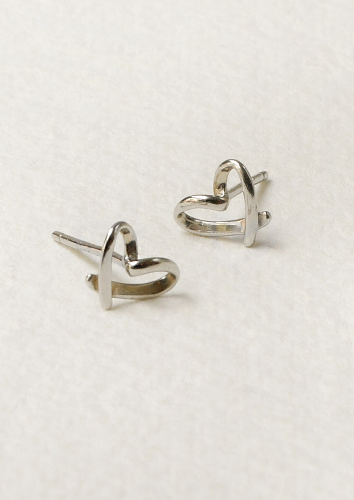 A pair of sterling silver stud earrings that are bent in the shape of hearts.