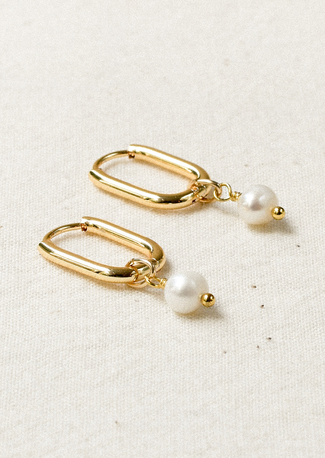 A pair of gold oval hoop earrings with a dangling freshwater pearl charm.
