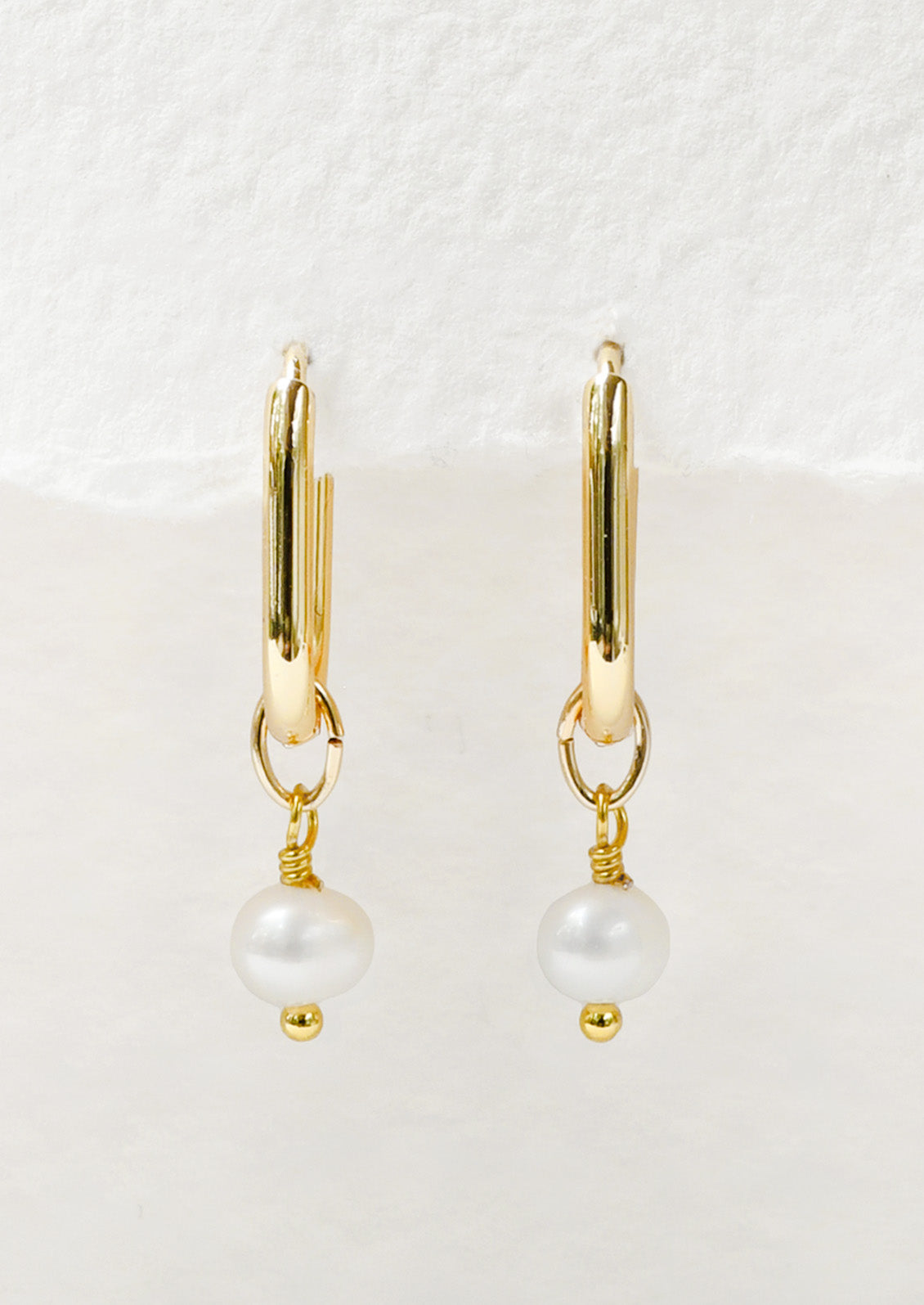 A pair of gold oval hoop earrings with a dangling freshwater pearl charm.