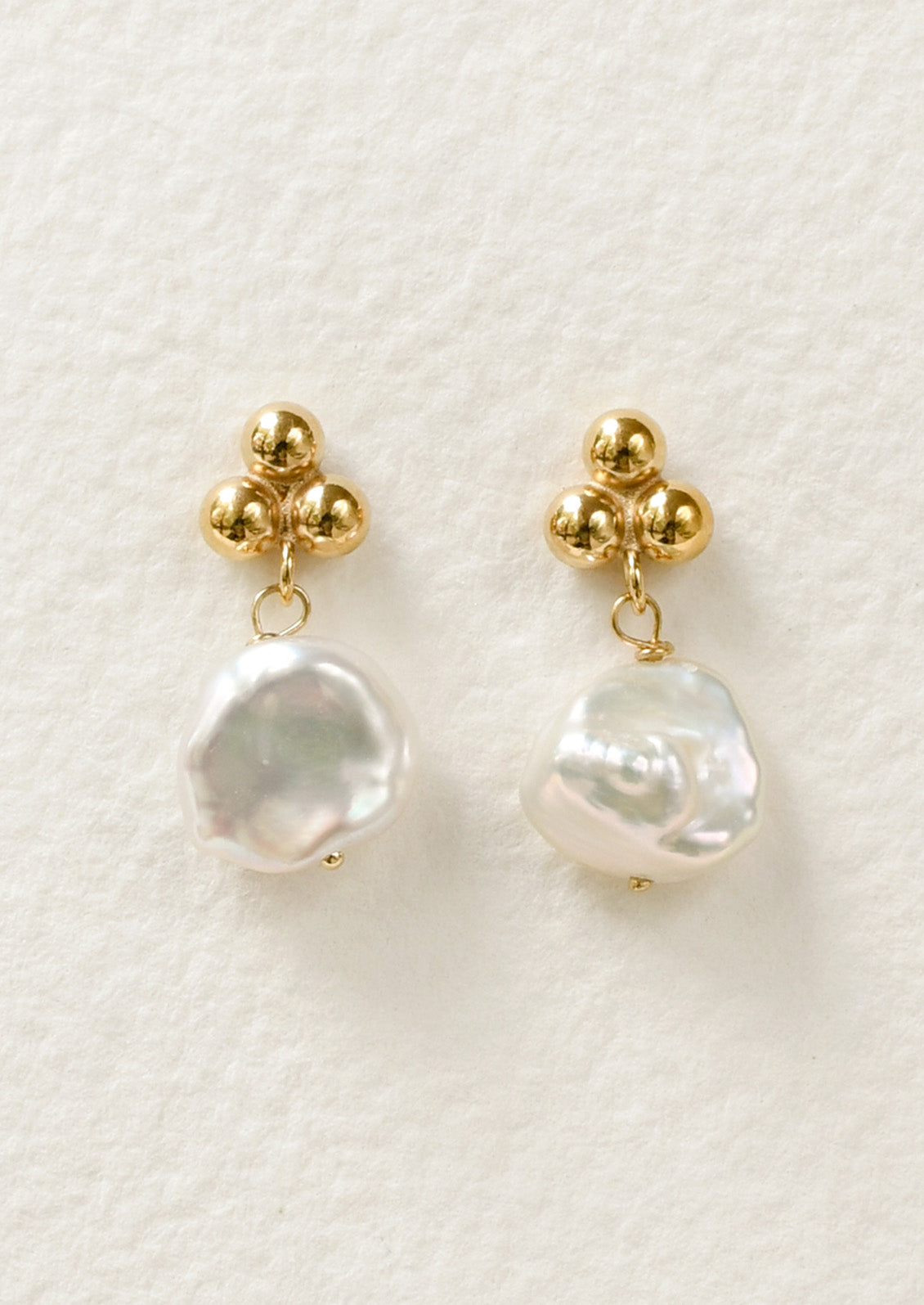 A pair of stud earrings featuring three round dots at the top and a dangling freshwater pearl.