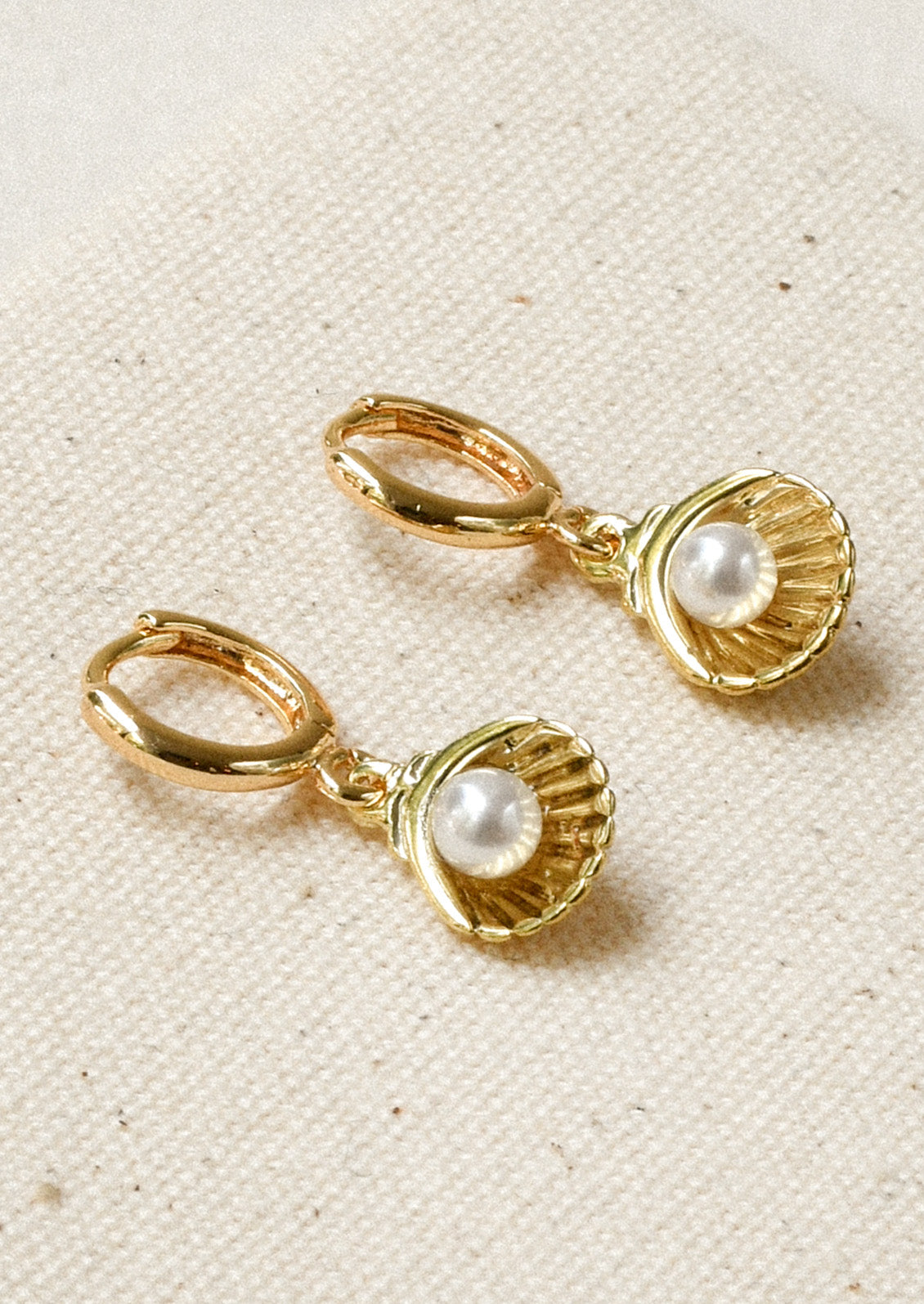 A pair of gold hoops with a dangling shell charm with a faux pearl in the center.