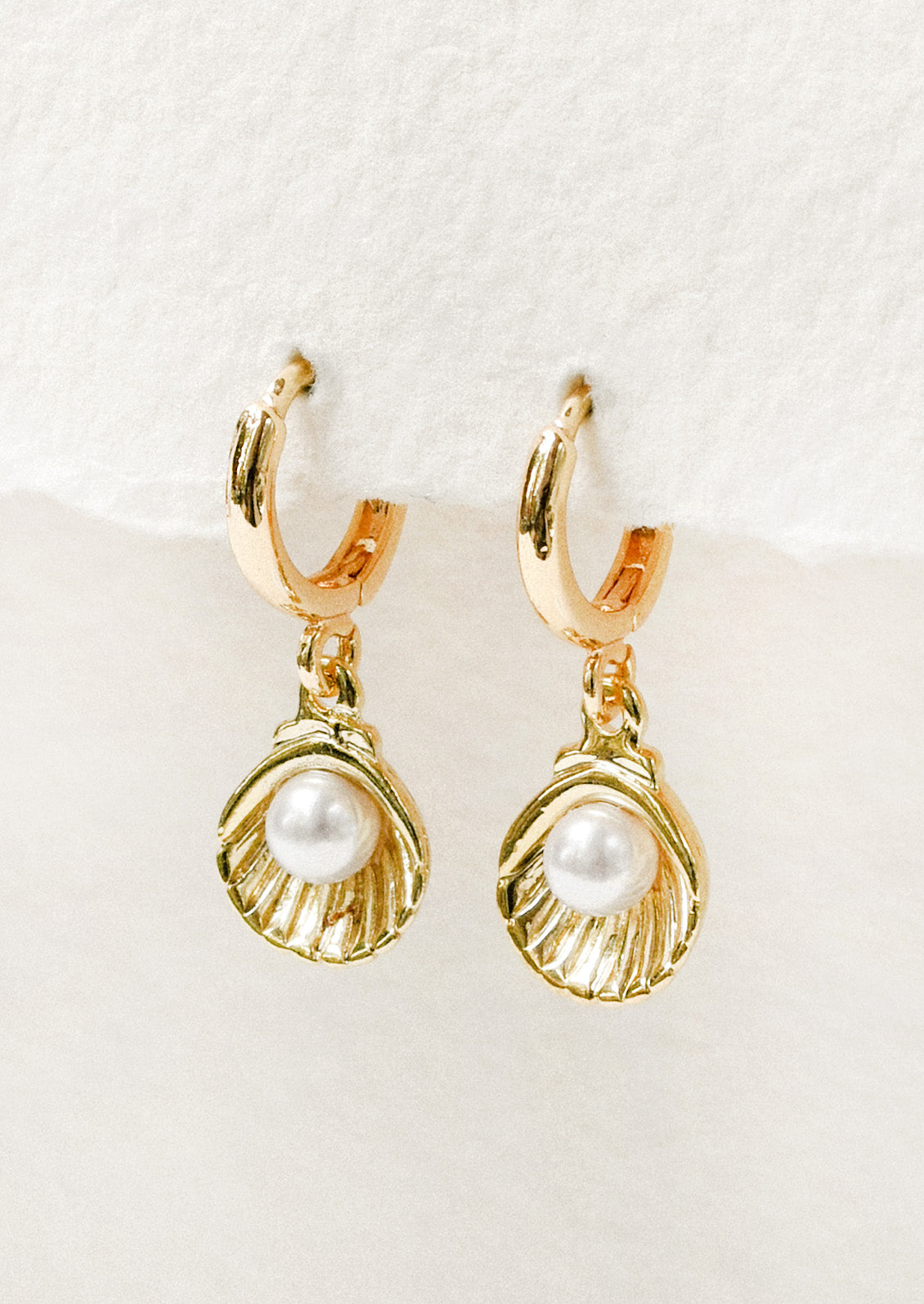 A pair of gold hoops with a dangling shell charm with a faux pearl in the center.