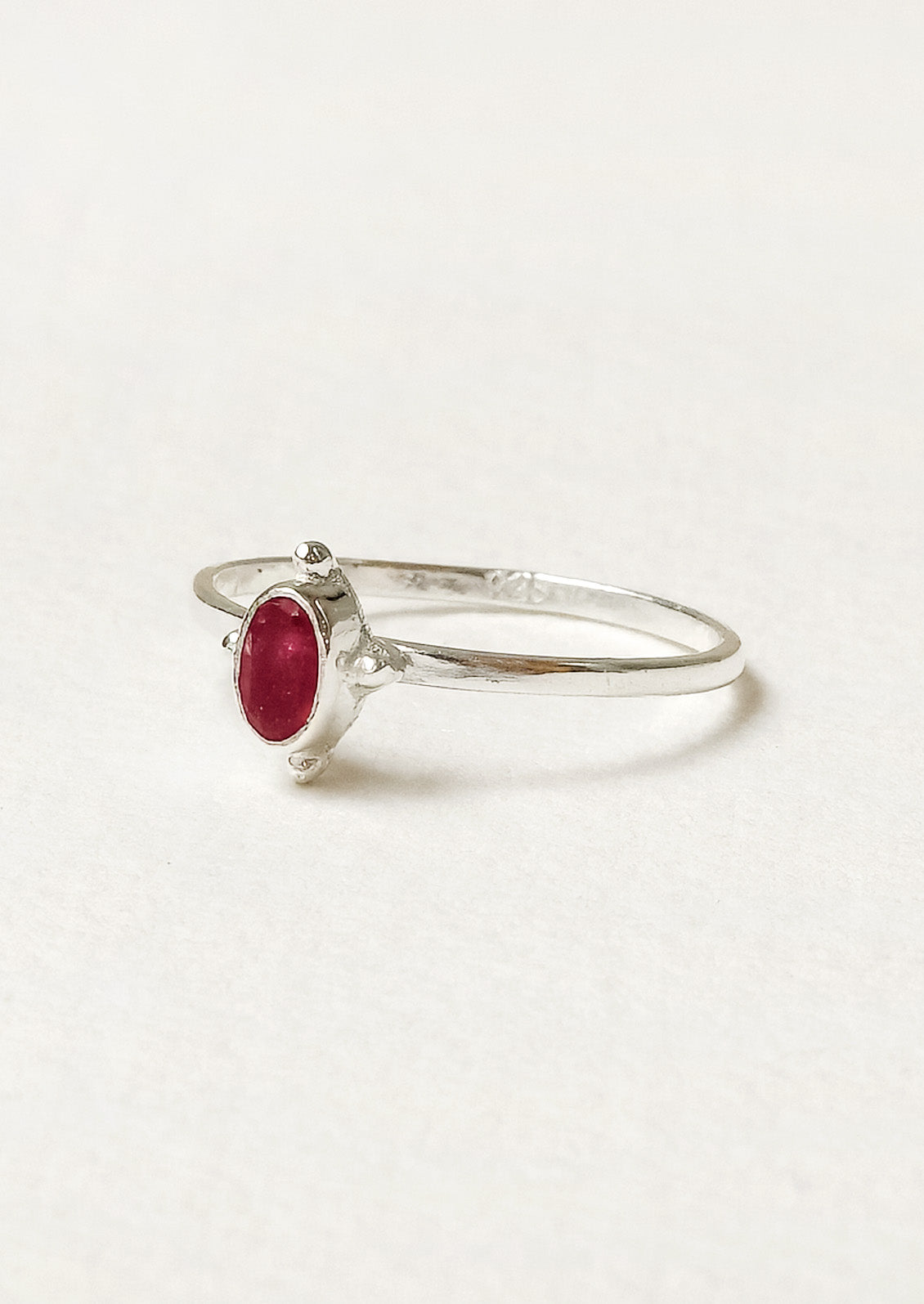 Side view of a sterling silver ring with a thin band and a small oval ruby stone in the center.