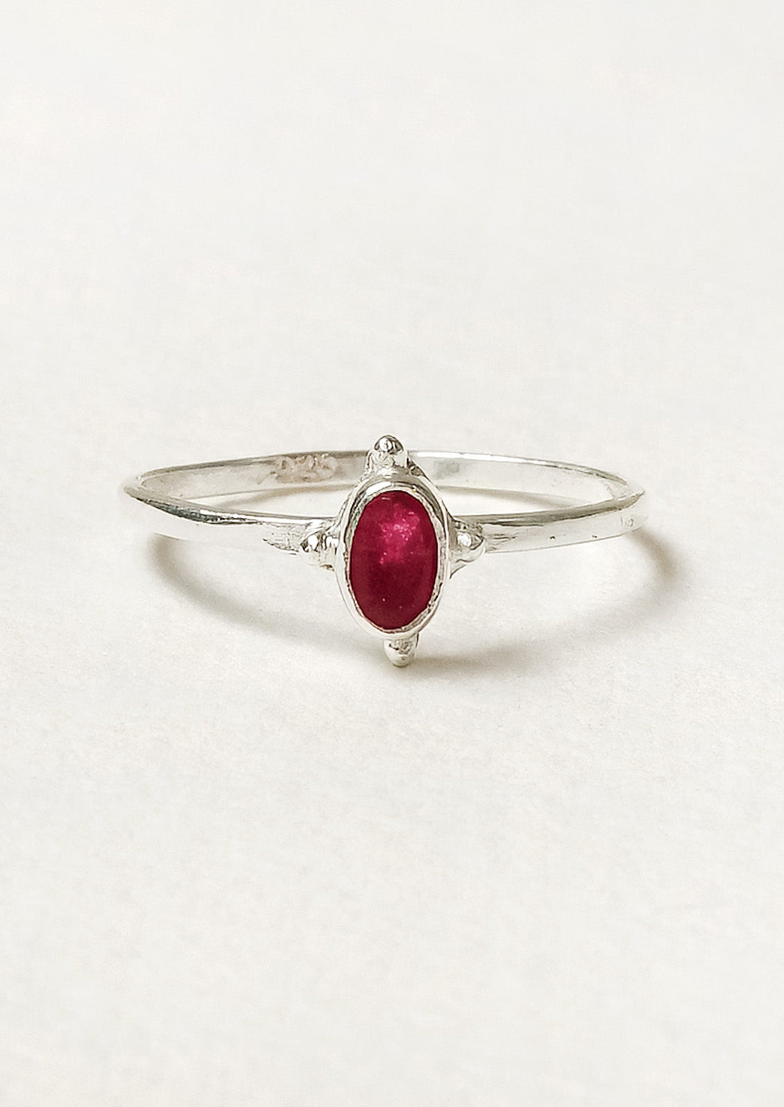 A sterling silver ring with a thin band and a small oval ruby stone in the center.