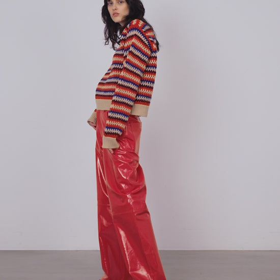 A woman wearing a crochet knit striped sweater in cream with orange, maroon and blue stripes.