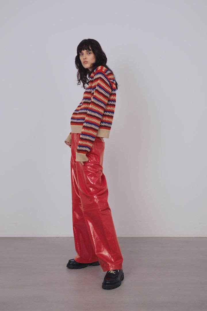 A woman wearing a crochet knit striped sweater in cream with orange, maroon and blue stripes.
