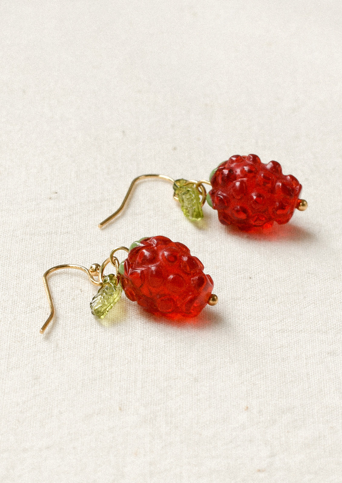 A pair of gold dangling earrings with dangling raspberry charms.