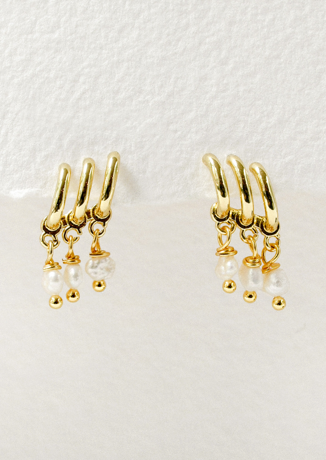 A pair of gold earrings featuring three half hoop and three faux pearls dangling from each earring.