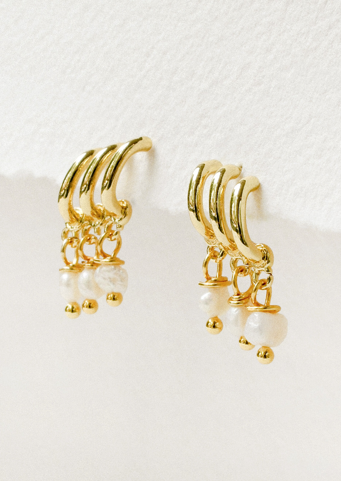 A pair of gold earrings featuring three half hoop and three faux pearls dangling from each earring.
