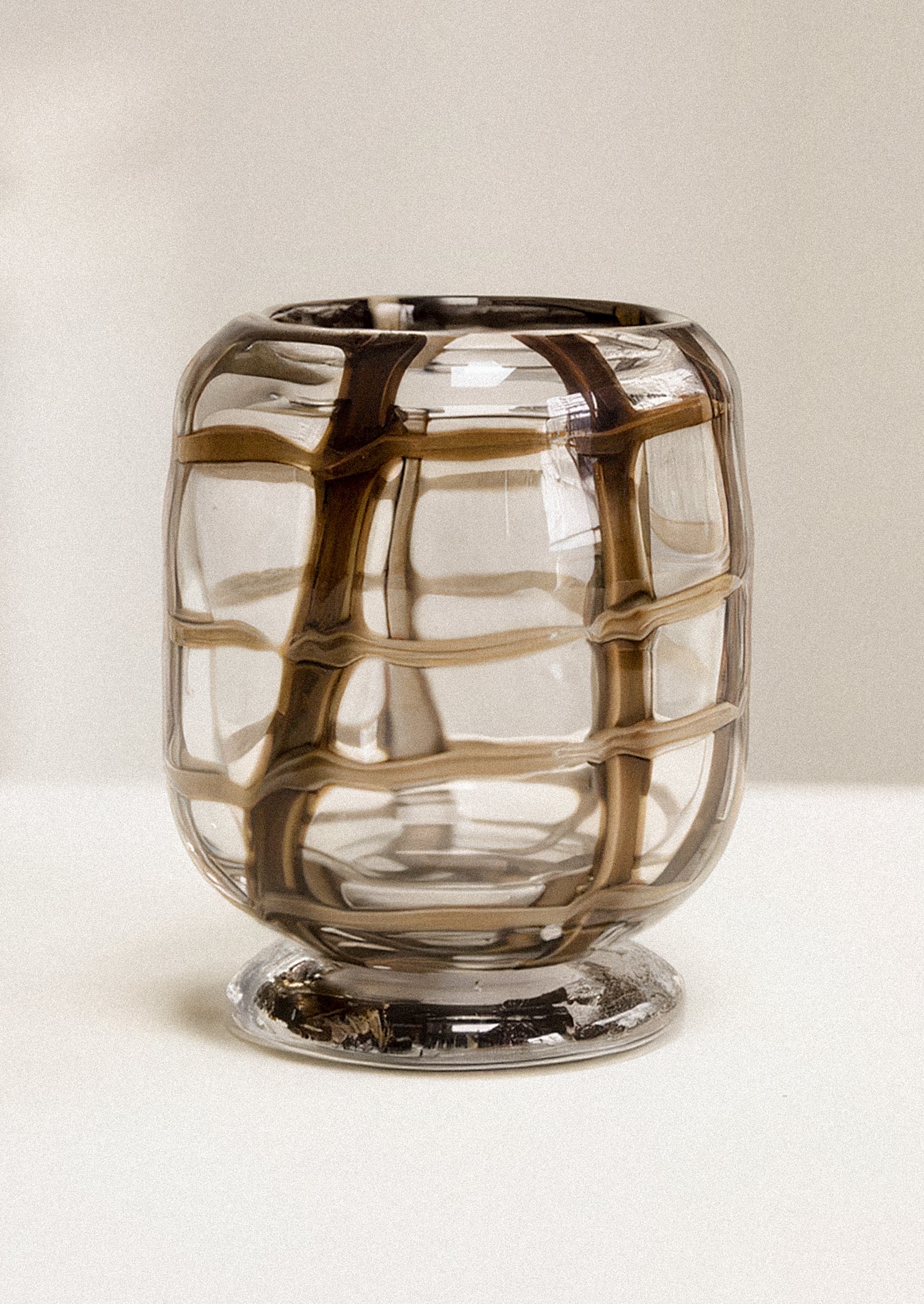 A clear glass vase with a grid-like pattern created by dark brown and black swirled glass, set against a neutral light beige background.