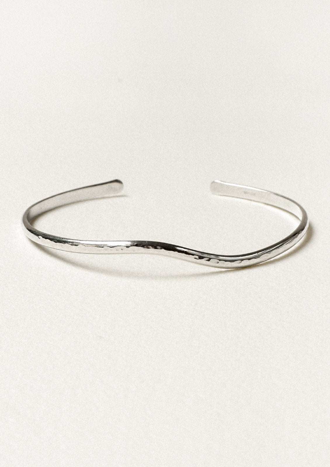A minimal silver cuff bracelet with a wave-like design.
