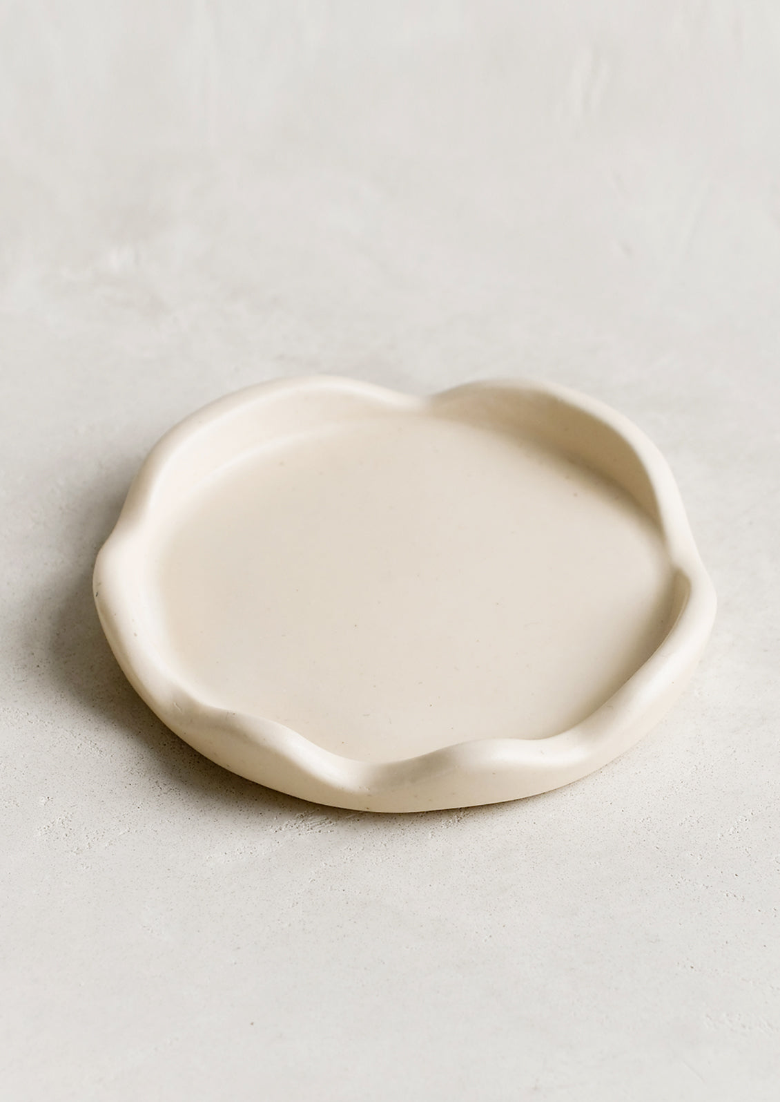 A cream resin coaster with curvy scalloped edges.