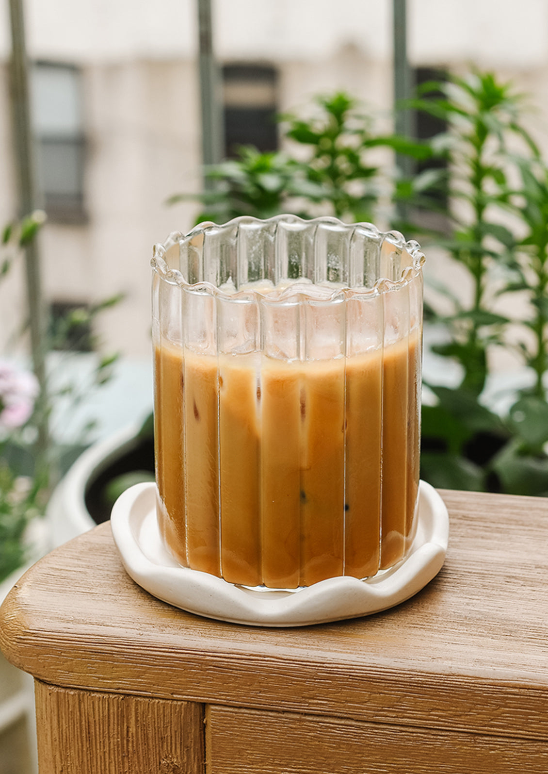 A glass cup of iced coffee on a scalloped coaster.