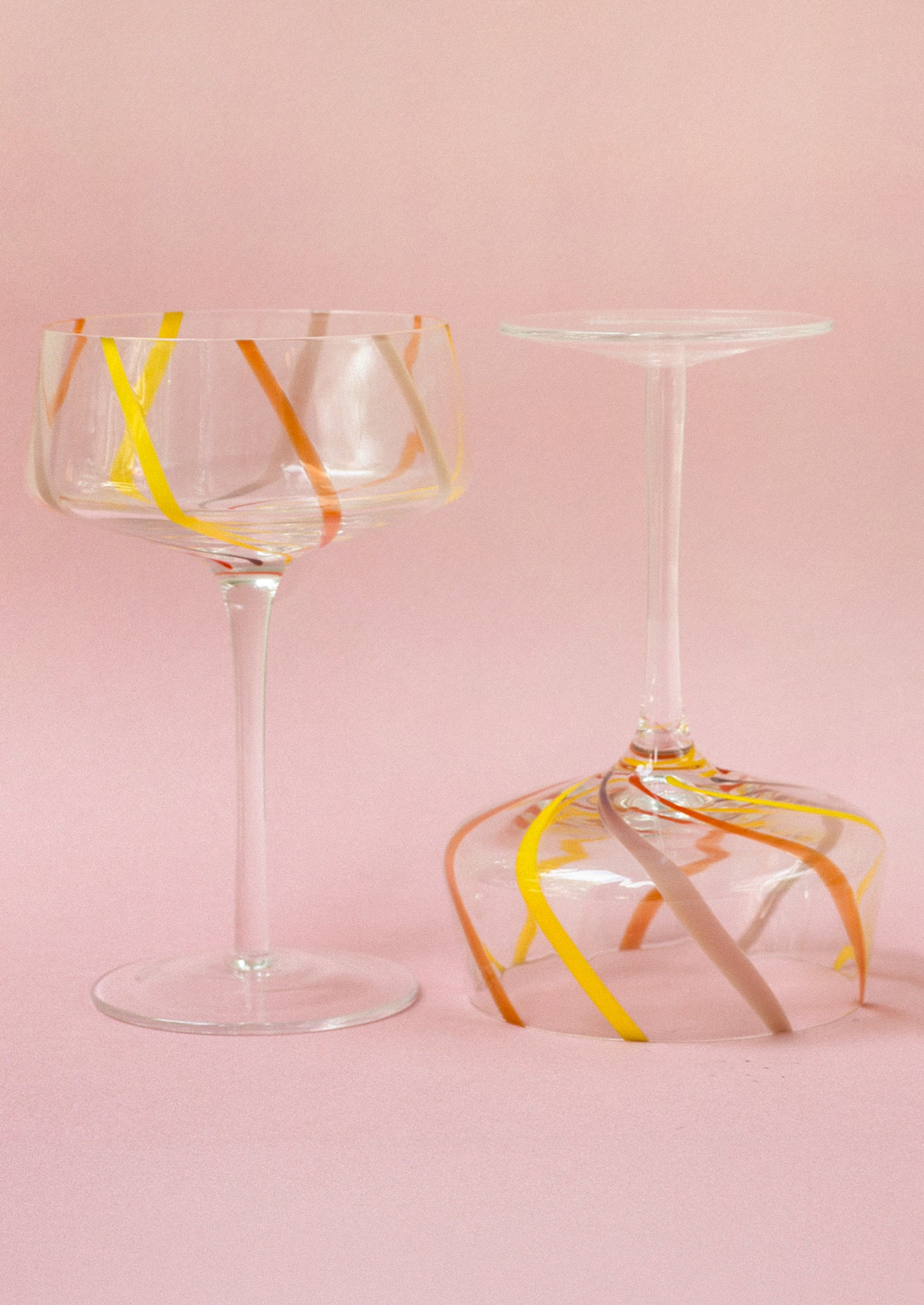 Two glass tumblers with colorful abstract designs on a pink background
