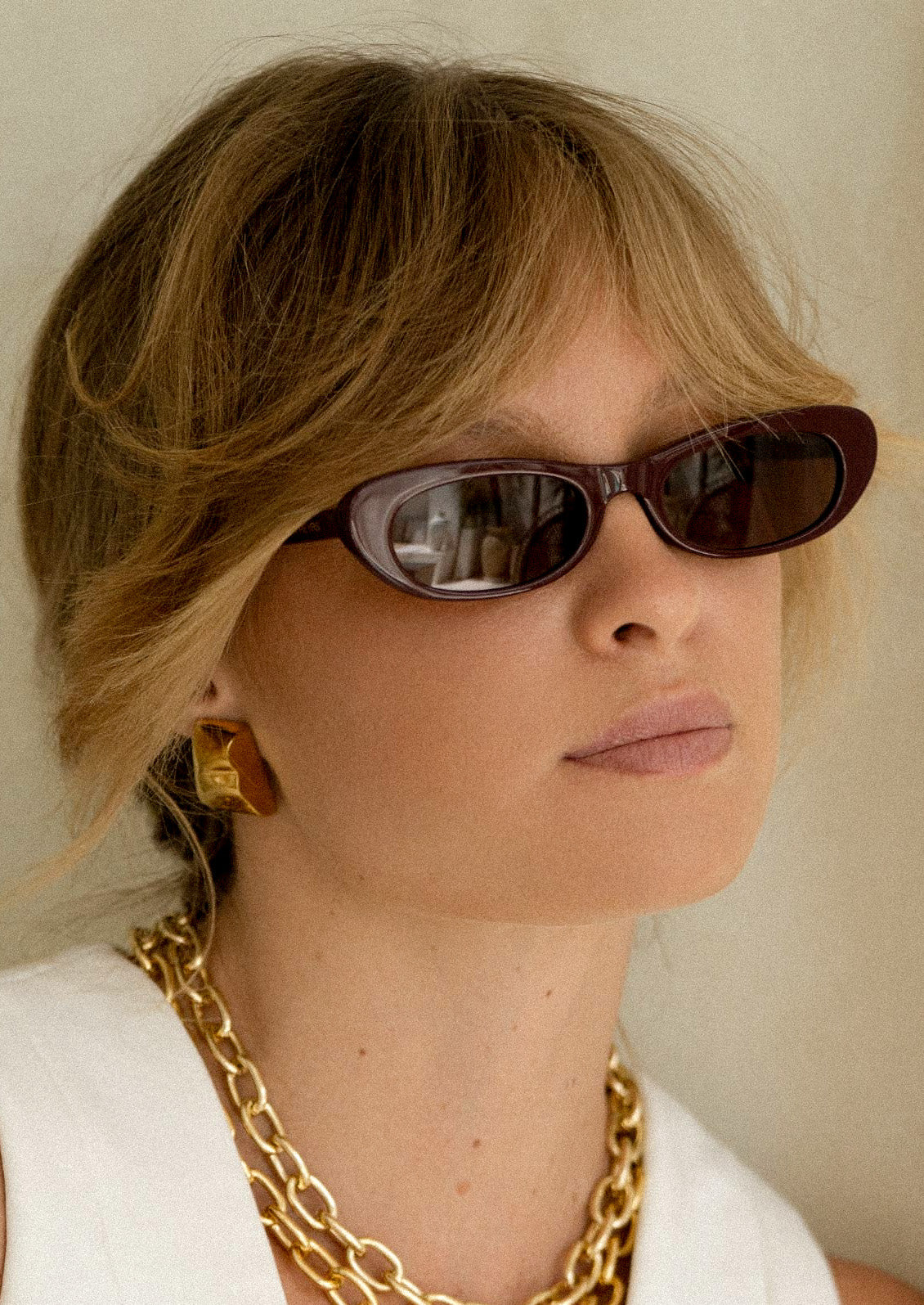 A woman wearing a pair of cat eye sunglasses with burgundy frames and brown tinted lenses.