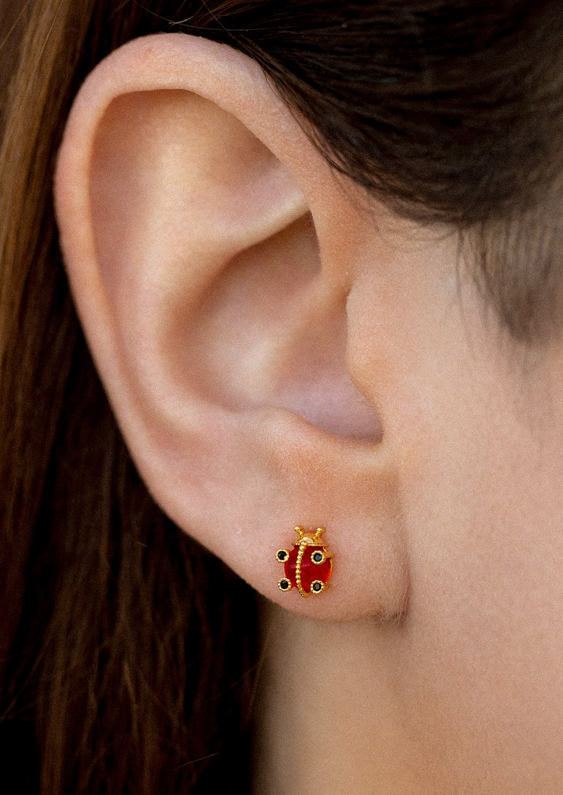 A woman wearing a gold plated earring in the shape of ladybug.