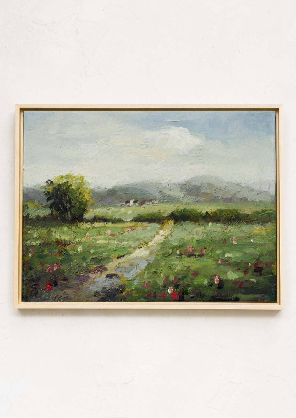 A framed original landscape oil painting of a green meadow with flowers.