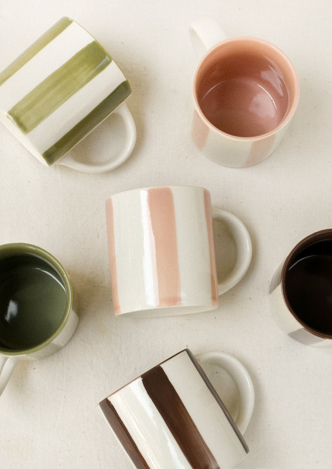 An assortment of small ceramic espresso cups with pink, green and brown stripes.