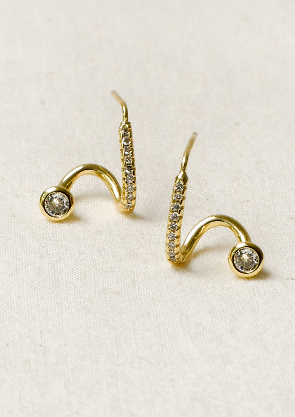 A pair of gold earrings in a unique sculpted design adorned with tiny cubic zirconias along the front.