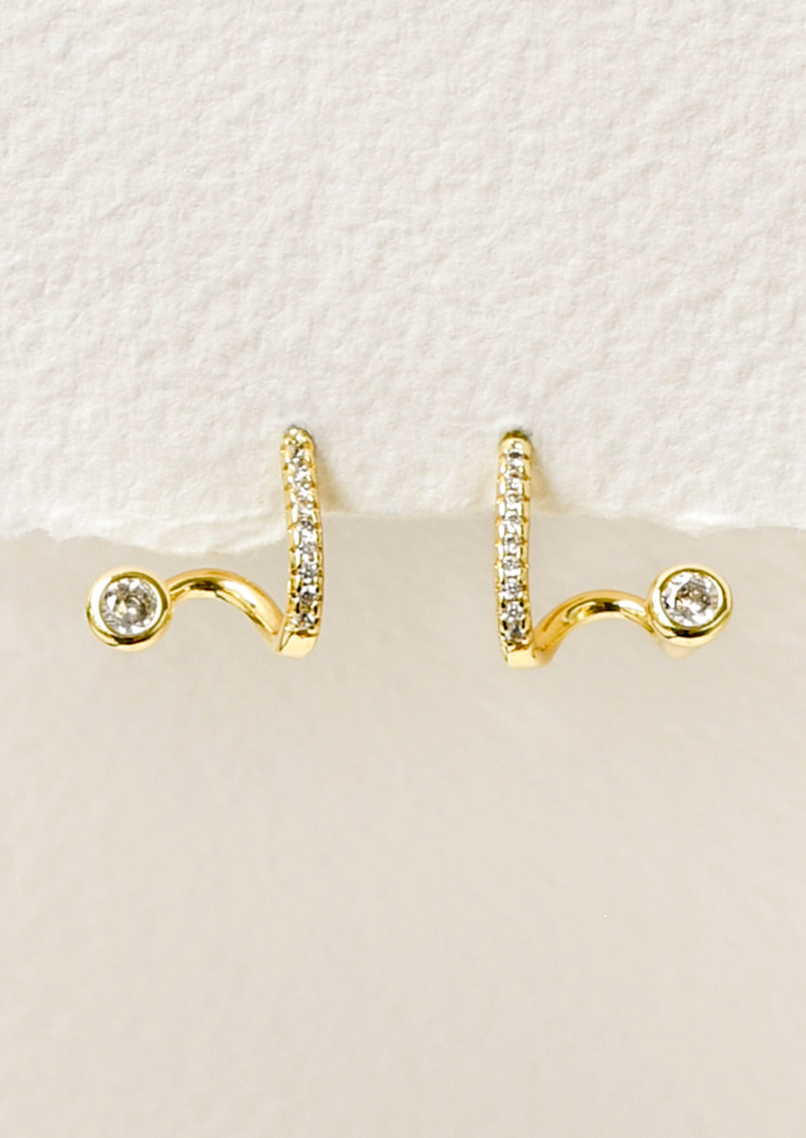 A pair of gold earrings in a unique sculpted design adorned with tiny cubic zirconias along the front.
