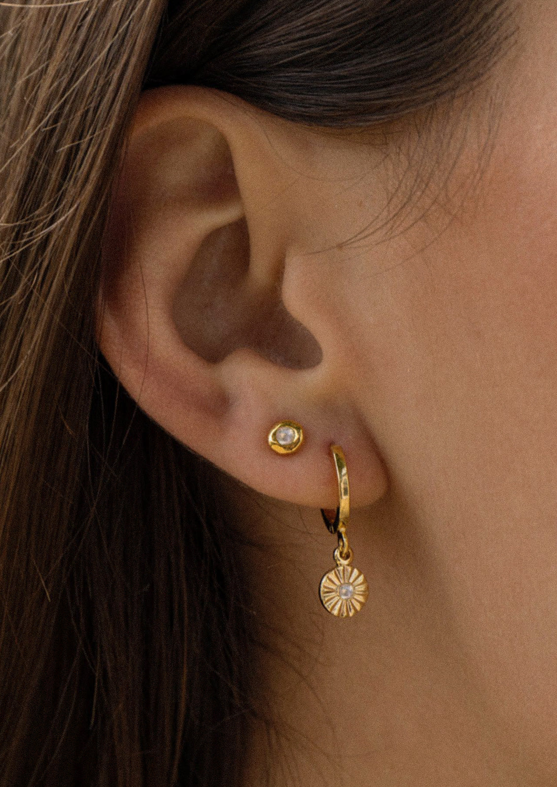 A woman wearing two gold earrings, one stud earring and one hoop earring.