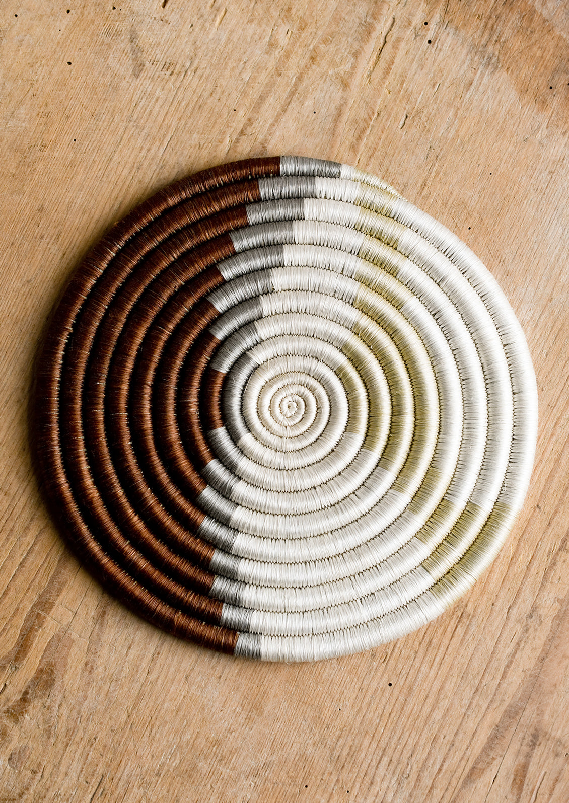 A woven sweetgrass trivet with geometric pattern in brown, grey, white and tan.