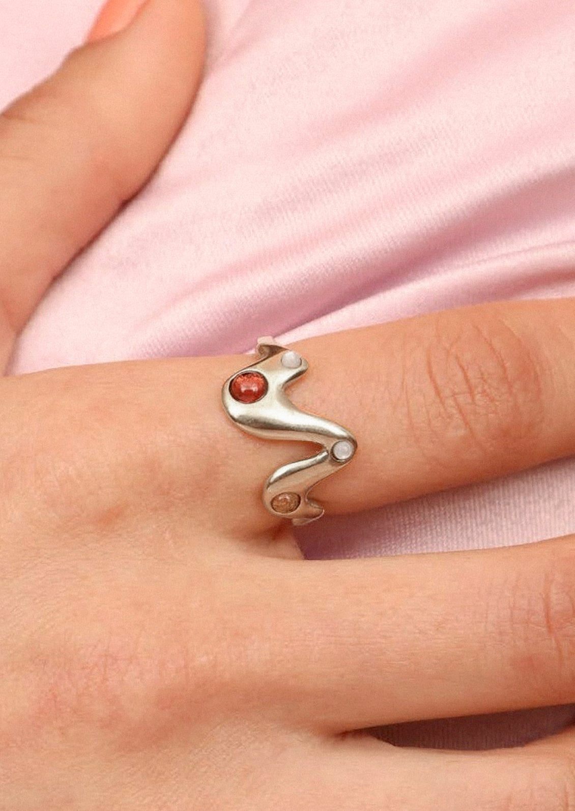 A hand with a sterling silver ring in a zigzag shape adorned with mother of pearls, garnet, and yellow citrine gems on its index finger.