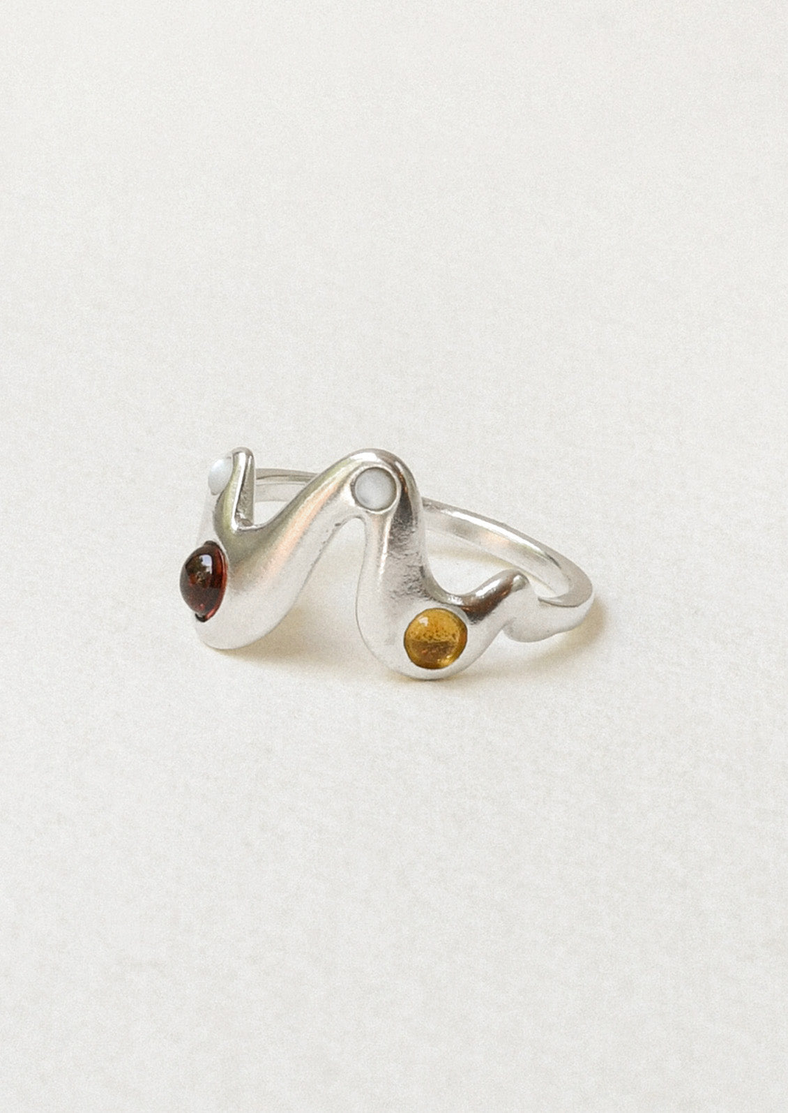 A sterling silver ring in a zigzag shape adorned with mother of pearls, garnet, and yellow citrine gems.