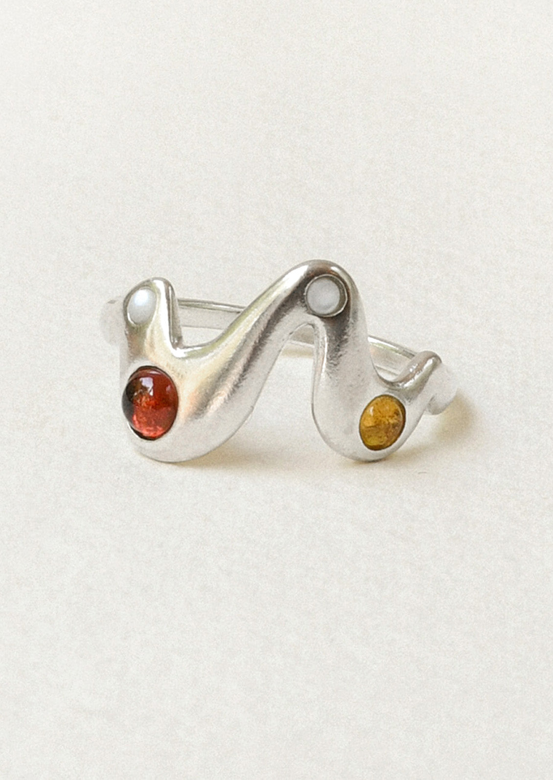 A sterling silver ring in a zigzag shape adorned with mother of pearls, garnet, and yellow citrine gems.