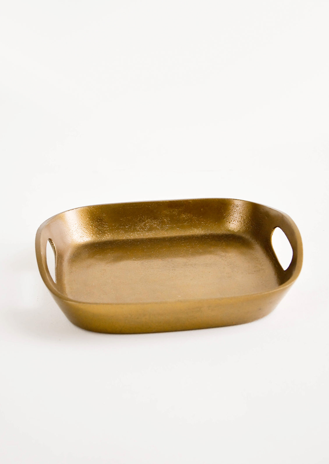 Square catchall tray in unpolished brass with raised sides, cutout handles at two sides