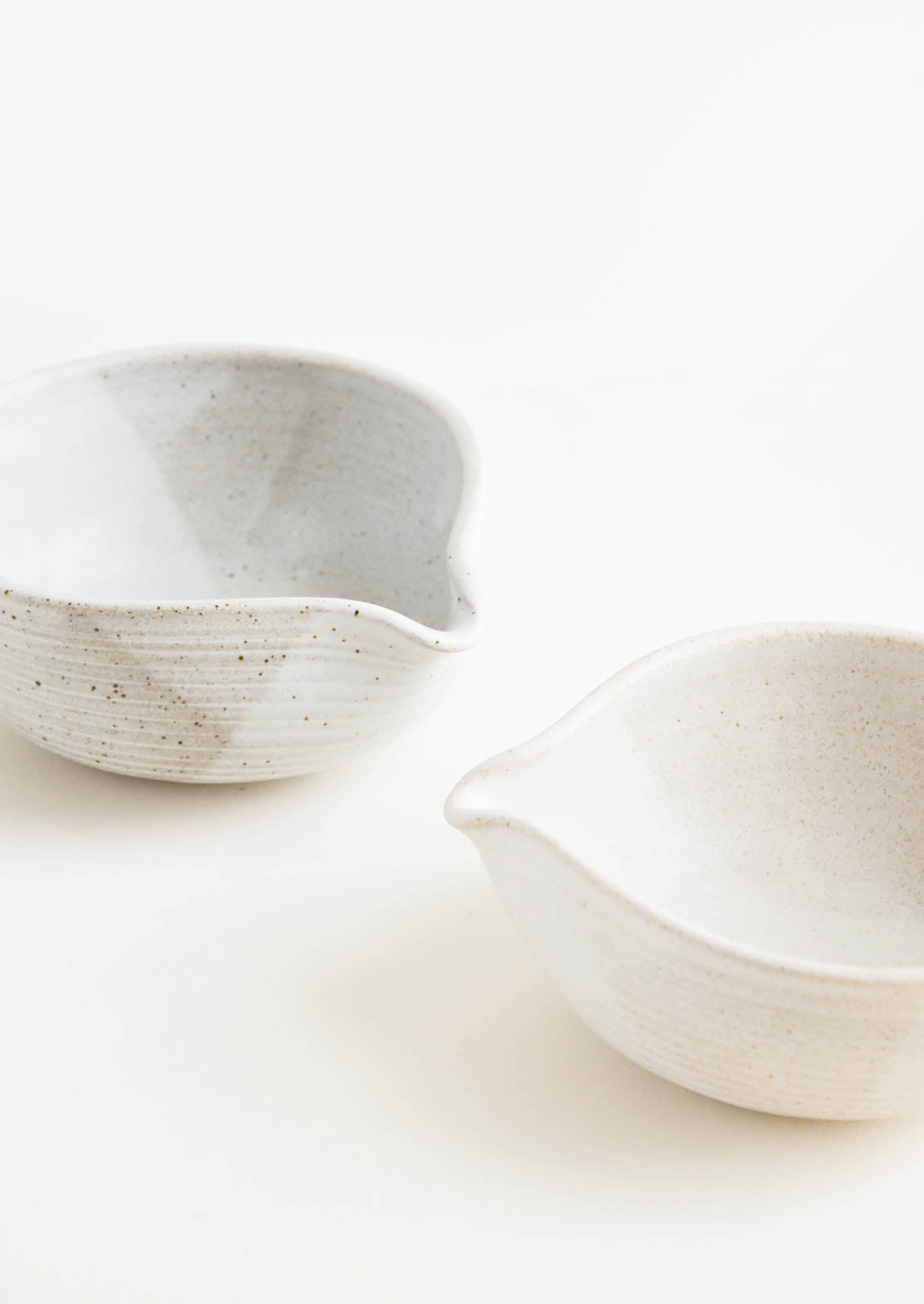Two ceramic spouted bowls in different shades of white.