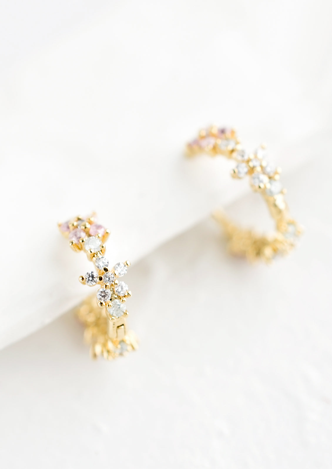 A pair of gold huggie hoop earrings with crystal flowers.