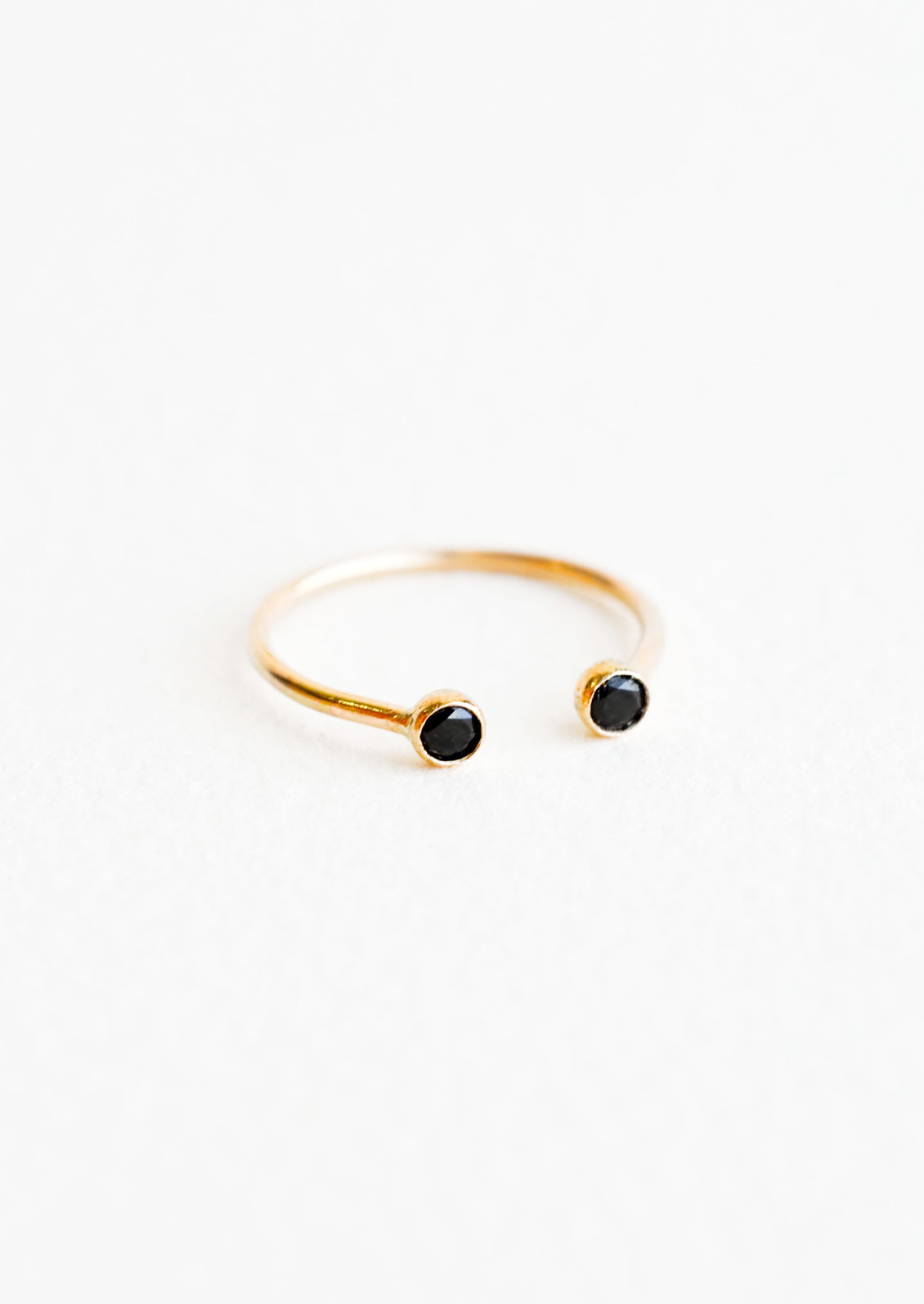 Yellow gold adjustable ring with opening at front and a black stone on each side of the opening.