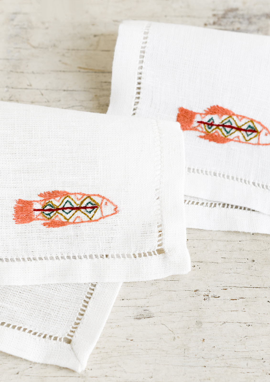 An white linen cocktail napkin with embroidered fish.
