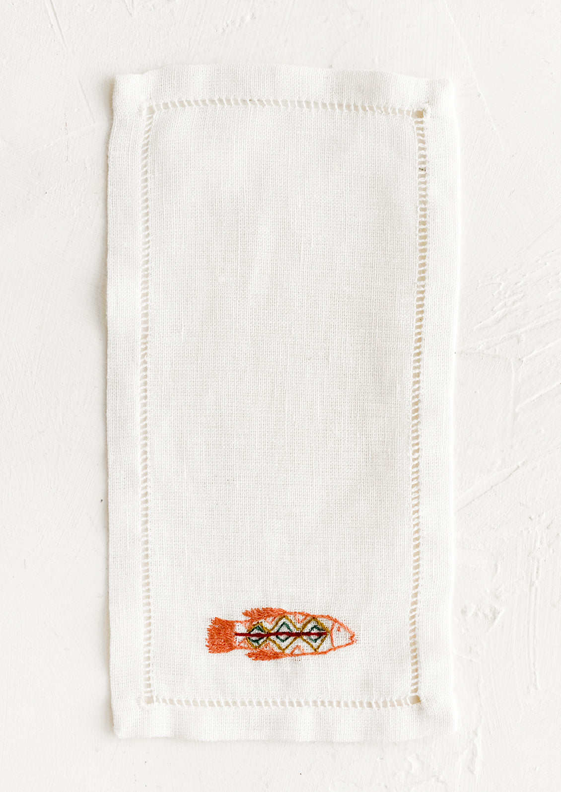 An white linen cocktail napkin with embroidered fish.