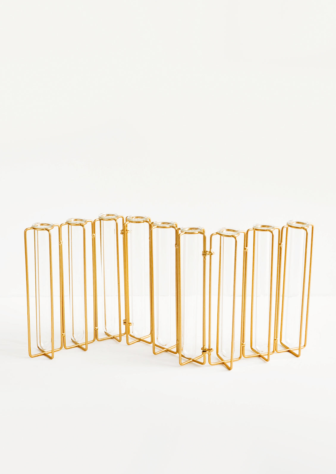 Multi-stem vase composed of nine glass vials side by side, resting inside individual compartments on a brass metal frame.