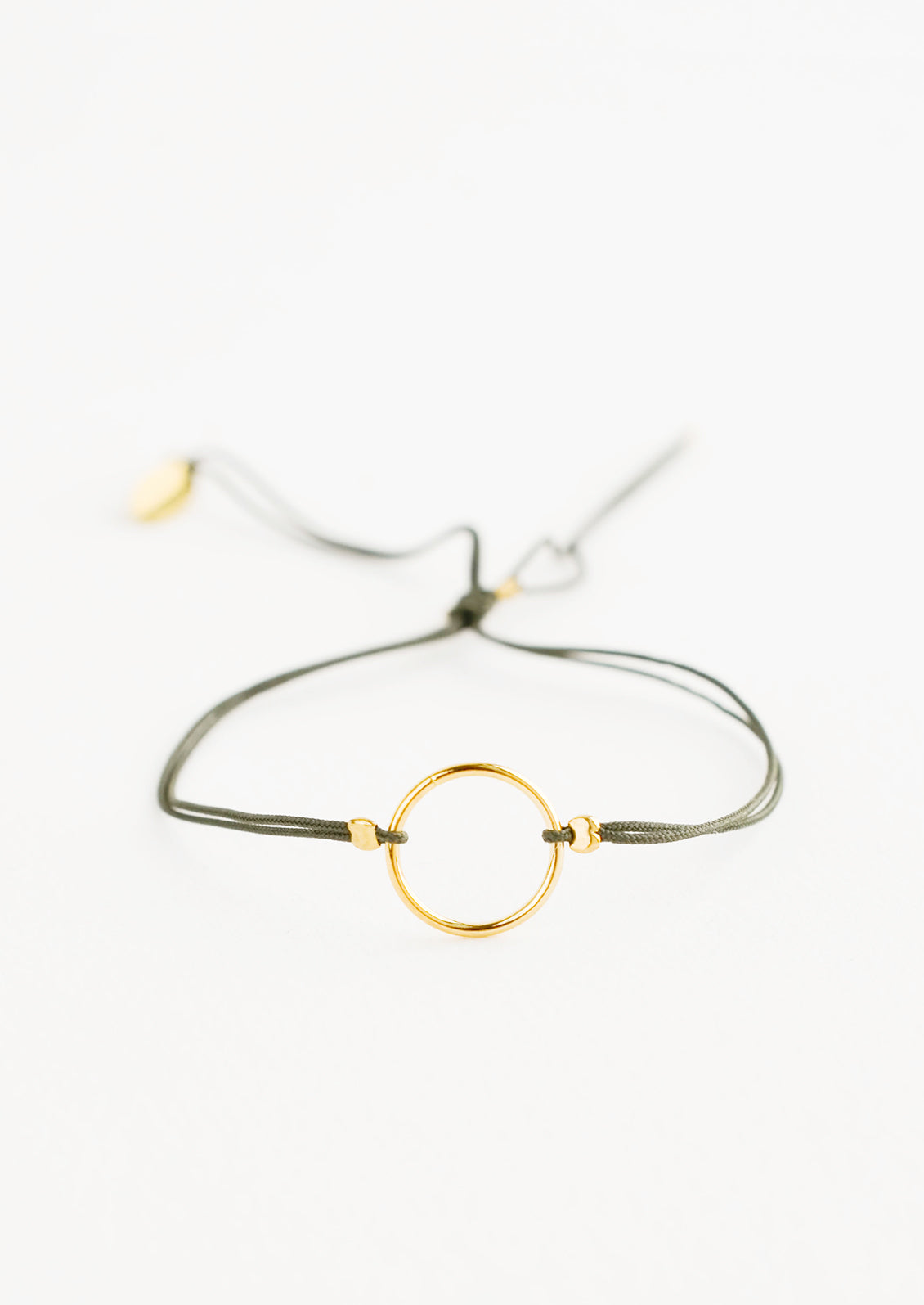 Bracelet with yellow gold circle charm centered on an adjustable green string.