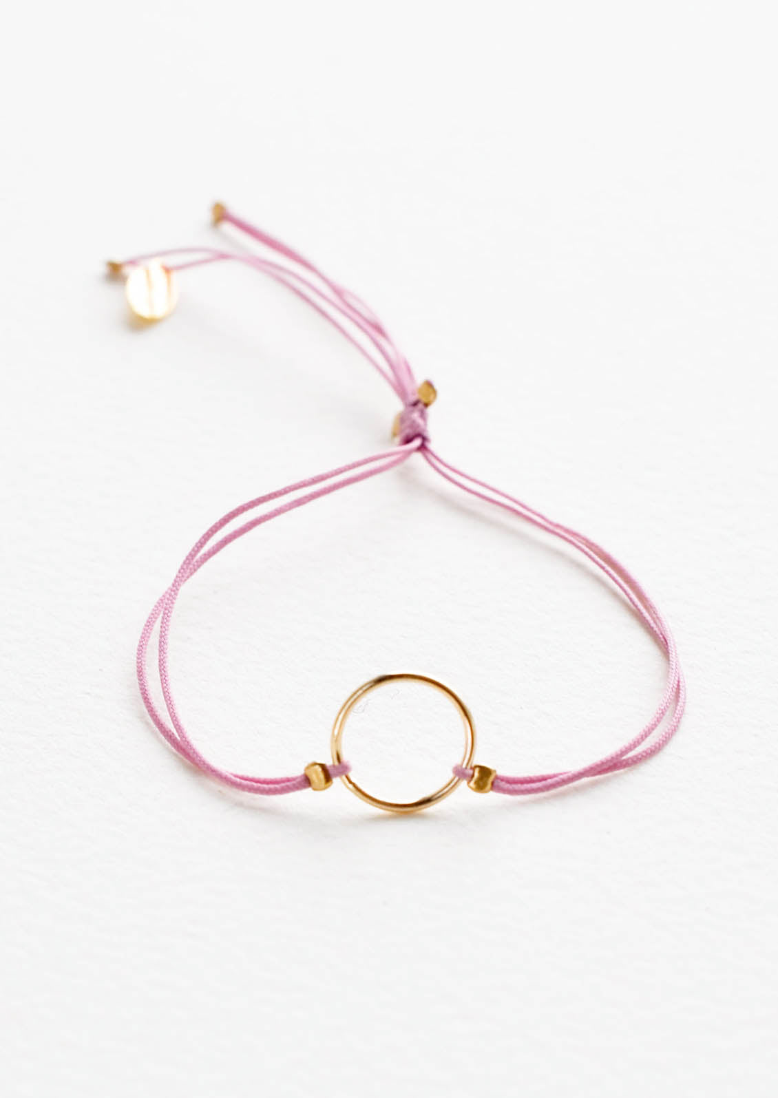 Bracelet with yellow gold circle charm centered on an adjustable purple string.