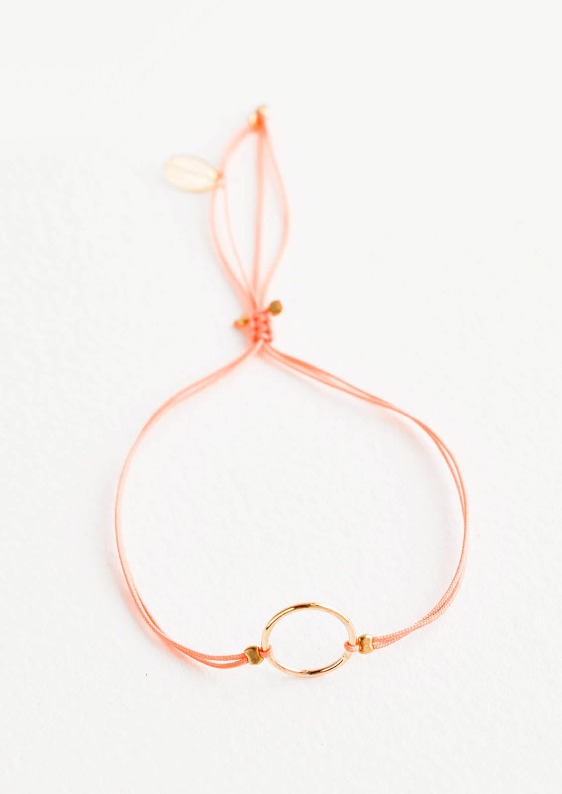 Bracelet with yellow gold circle charm centered on an adjustable peach string.