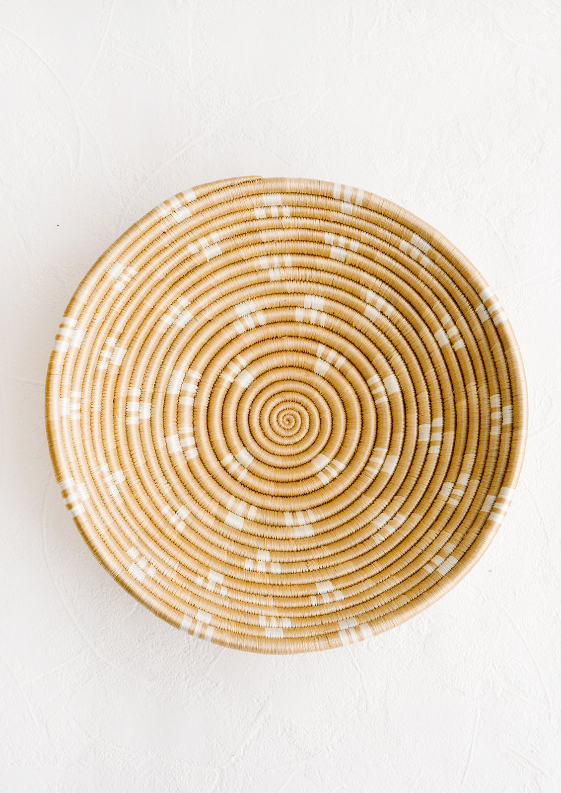 A round sweetgrass bowl in tan with white pattern.