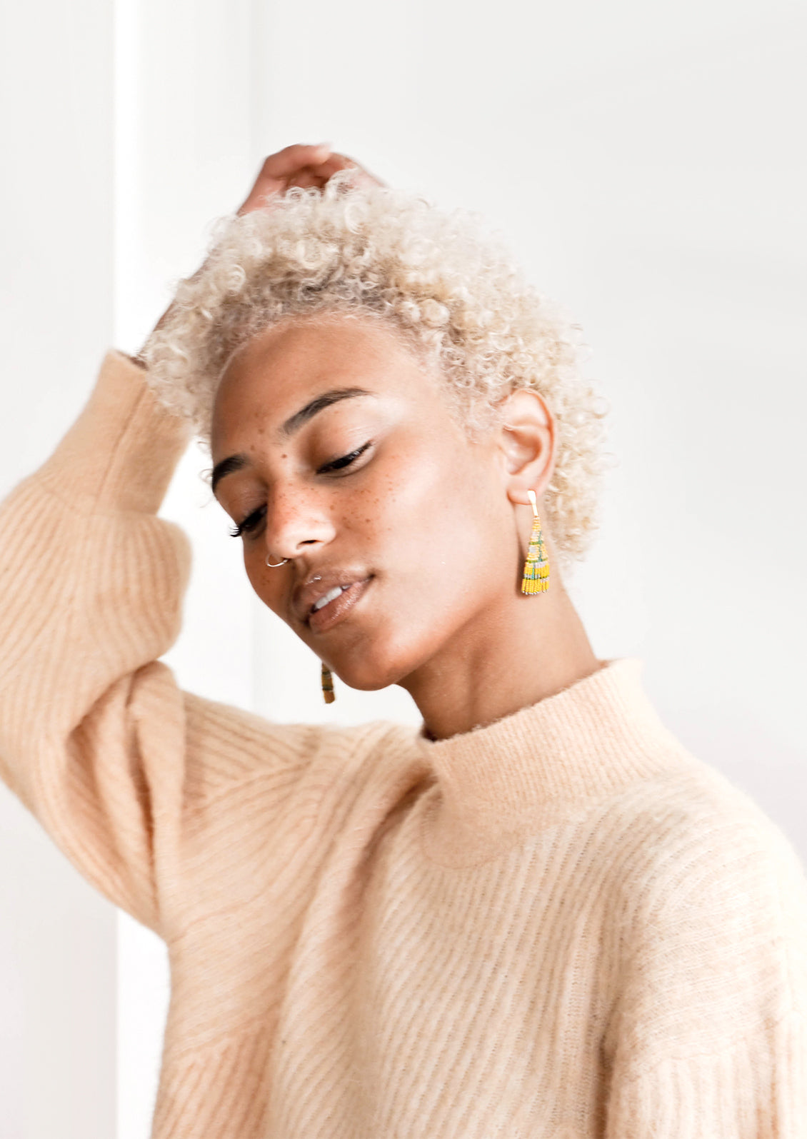 Model wears yellow triangle shaped beaded earrings and peach sweater.