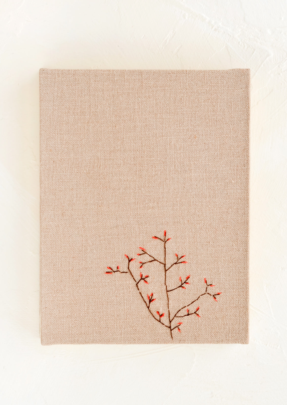 A mauve cloth covered journal with botanical embroidery detail.