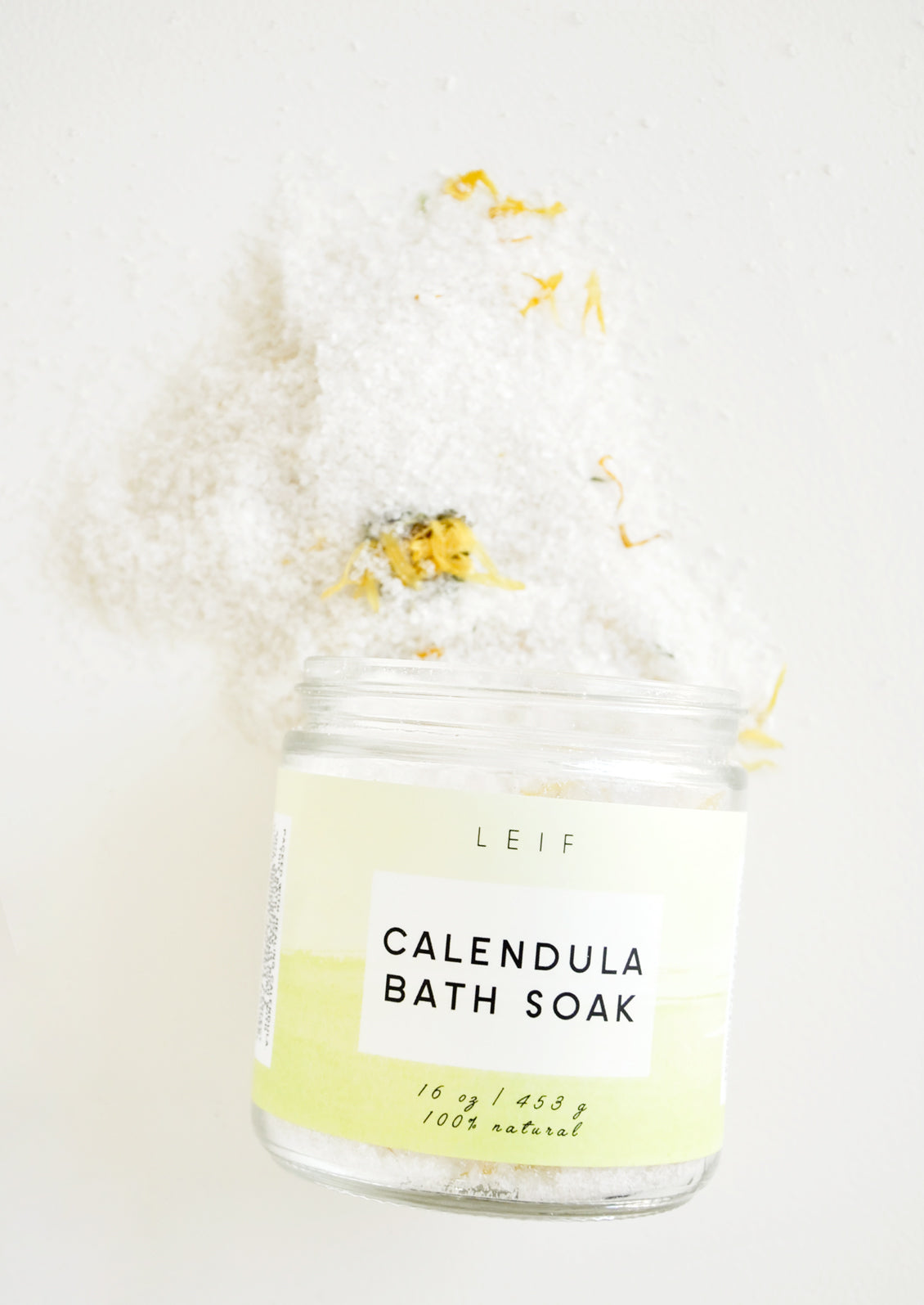 White powder with specks of yellow flowers spills out of a glass jar with a yellow-green label.