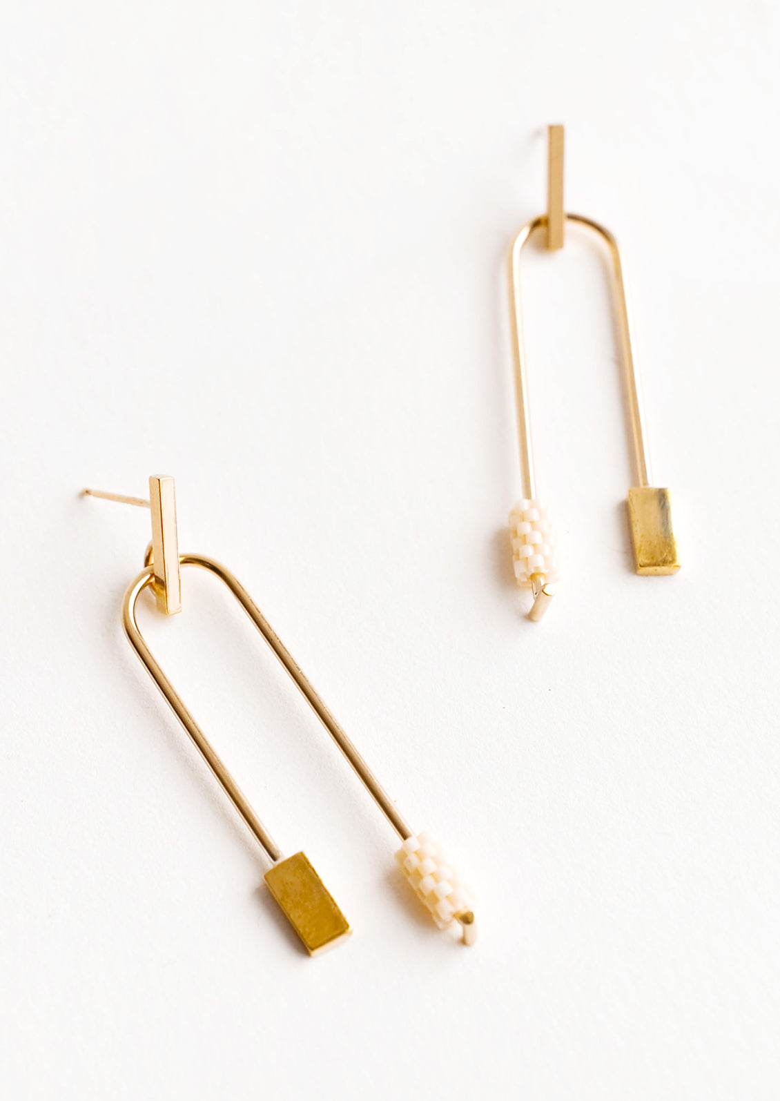 Post back gold earrings with curved arc featuring one cream color beaded end and one square gold end.